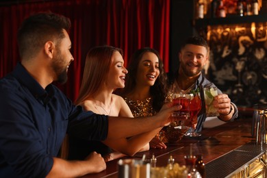 Photo of Happy friends clinking glasses with fresh cocktails at bar counter