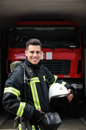 Photo of Portrait of firefighter in uniform with helmet near fire truck at station
