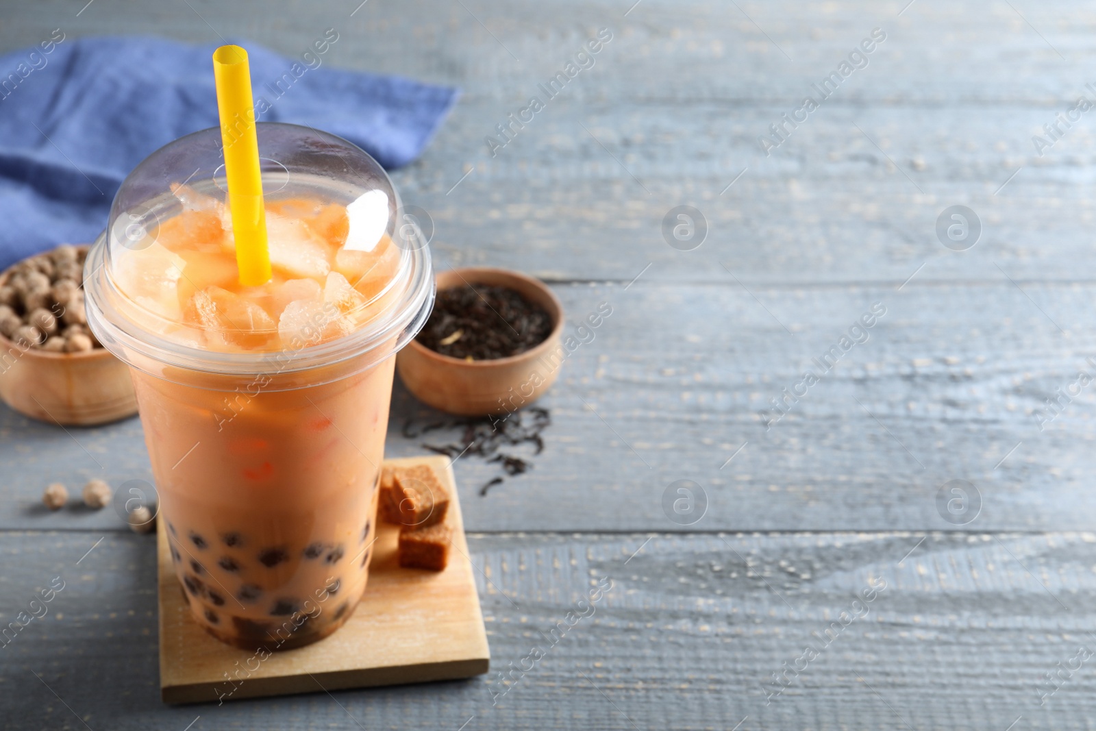 Photo of Tasty brown milk bubble tea in plastic cup on light blue wooden table. Space for text