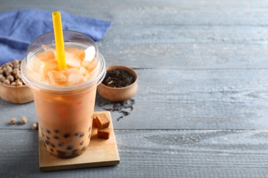 Photo of Tasty brown milk bubble tea in plastic cup on light blue wooden table. Space for text