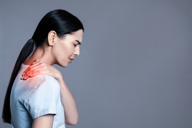 Woman suffering from shoulder pain on grey background. Space for text