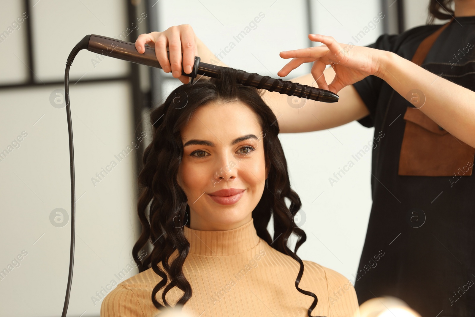 Photo of Hair styling. Hairdresser curling woman's hair in salon, closeup