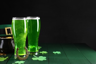 Photo of St. Patrick's day party. Green beer, leprechaun hat, pot of gold, horseshoe and decorative clover leaves on wooden table. Space for text