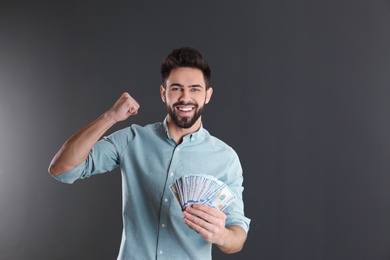 Portrait of happy young man with money on grey background. Space for text