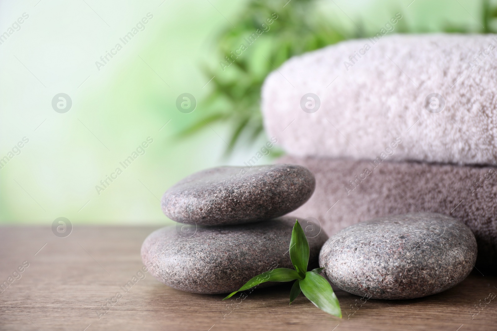 Photo of Composition with spa stones and towels on wooden table against blurred background. Space for text