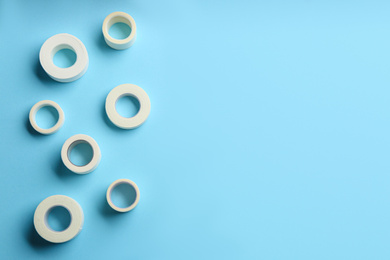 Photo of Sticking plaster rolls on light blue background, flat lay. Space for text