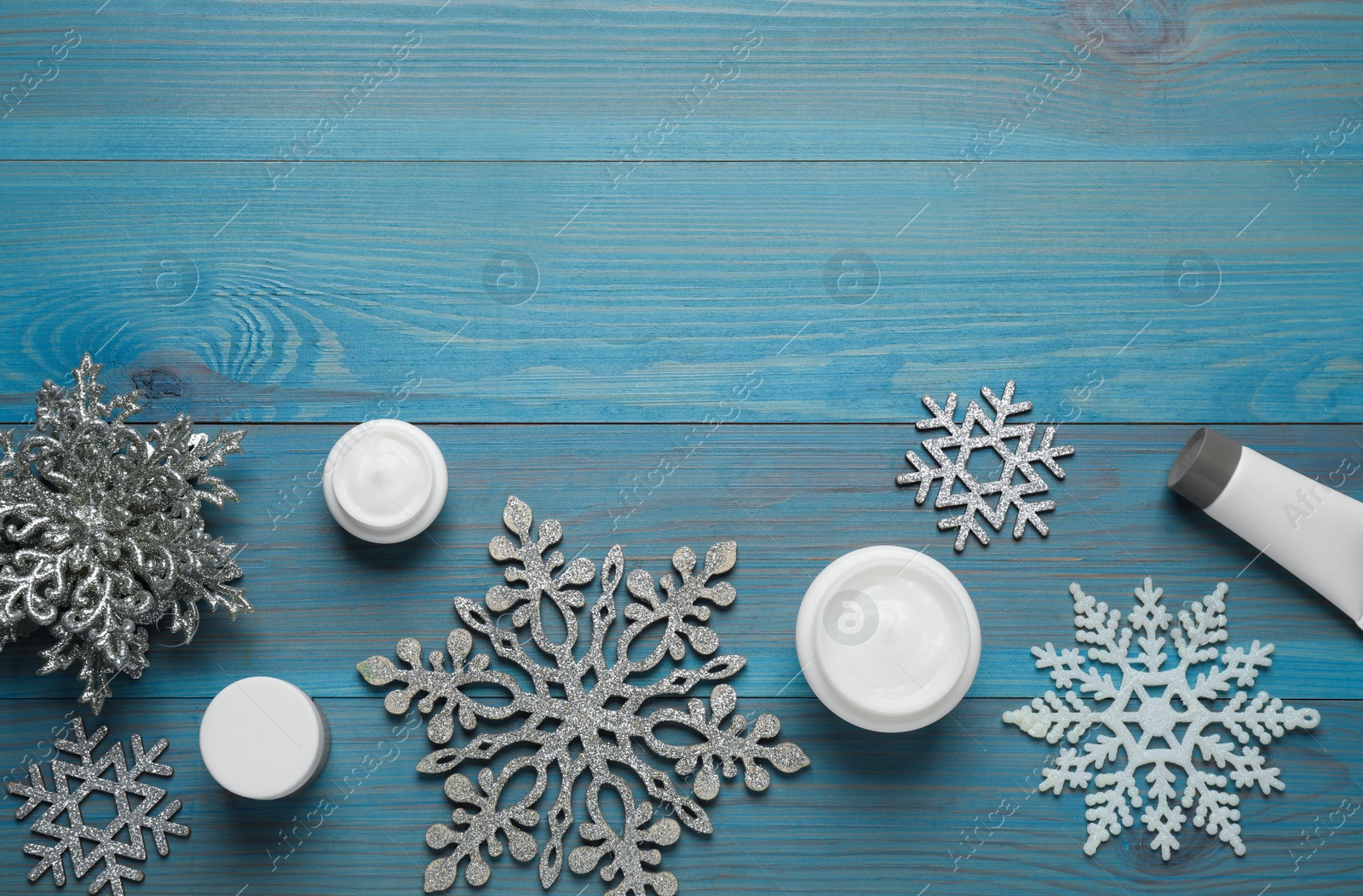 Photo of Flat lay composition with cosmetic products and snowflakes on turquoise wooden table, space for text. Winter skin care