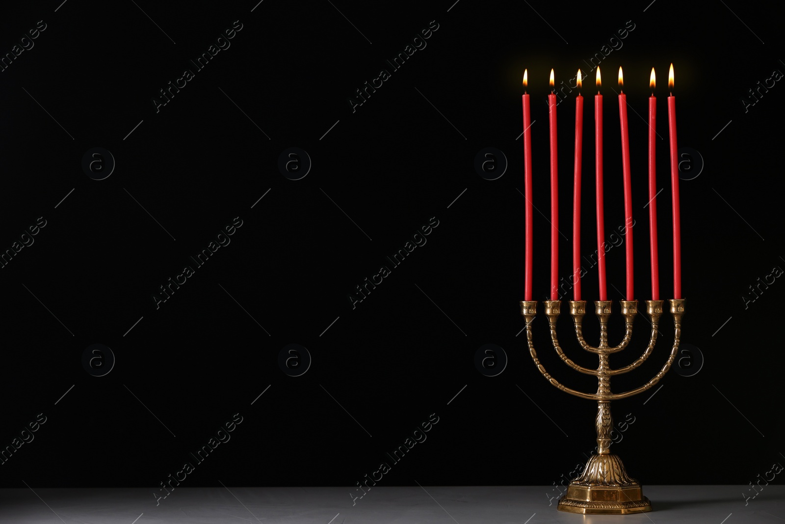 Photo of Golden menorah with burning candles on table against black background, space for text