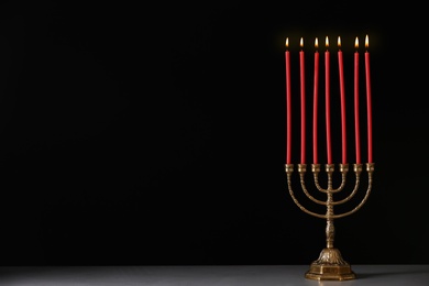 Photo of Golden menorah with burning candles on table against black background, space for text