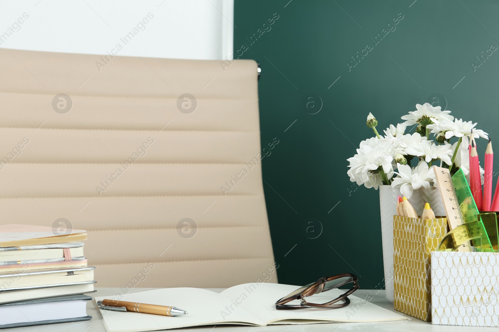 Photo of Flowers and stationery on table near chalkboard in classroom. Happy teacher's day