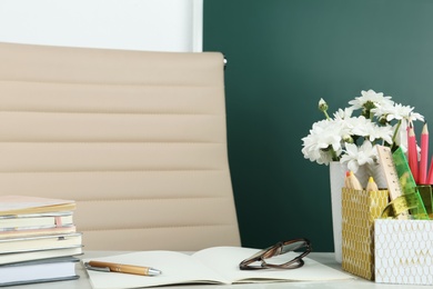 Flowers and stationery on table near chalkboard in classroom. Happy teacher's day