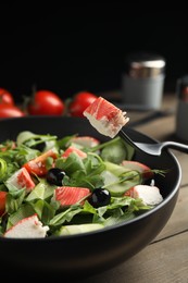 Photo of Delicious crab stick salad in bowl on wooden table, closeup