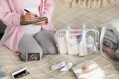 Photo of Pregnant woman preparing list of necessary items to bring into maternity hospital on bed, closeup