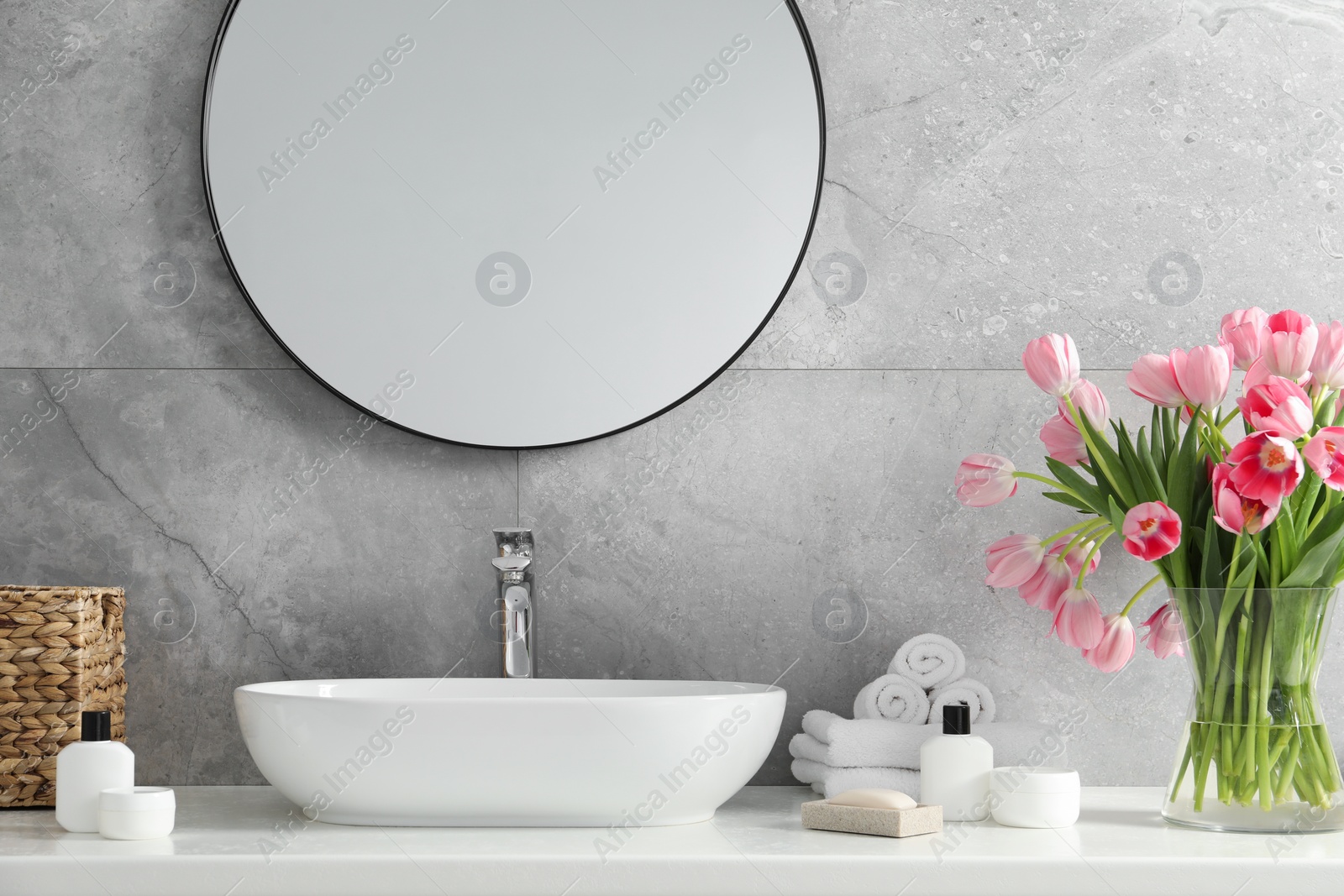 Photo of Vase with beautiful pink tulips and toiletries near sink in bathroom