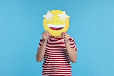 Photo of Woman holding emoticon with stars instead of eyes on light blue background