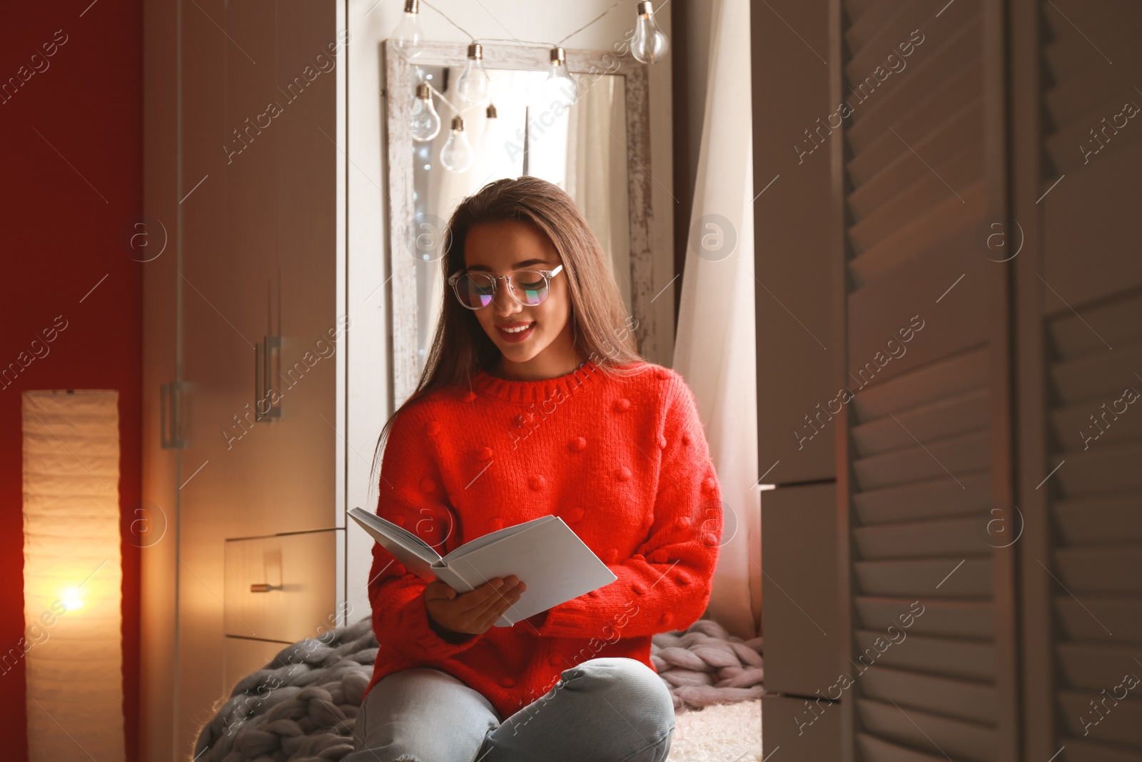 Photo of Young woman reading book near window at home. Winter season