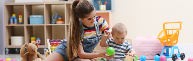 Image of Teen nanny and cute little baby playing with toys at home. Banner design 