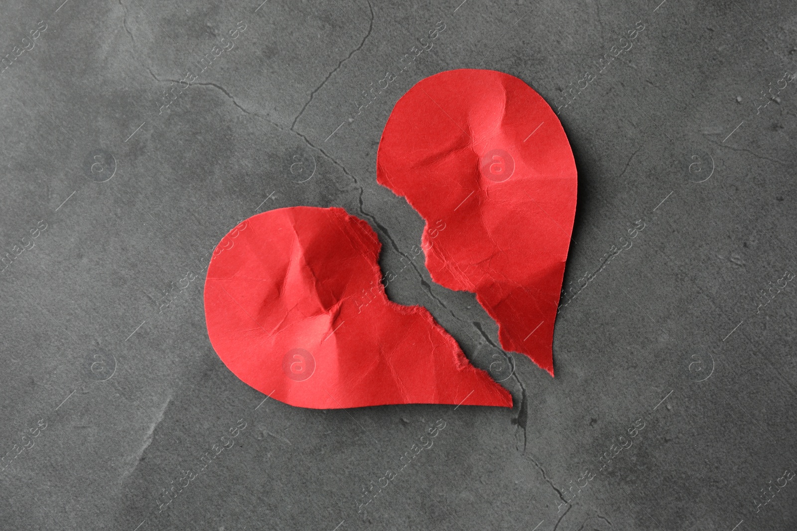 Photo of Halves of torn red paper heart on grey table, top view. Broken heart