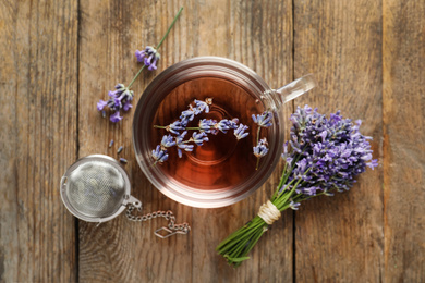 Photo of Fresh delicious tea with lavender, strainer and beautiful flowers on wooden table, flat lay