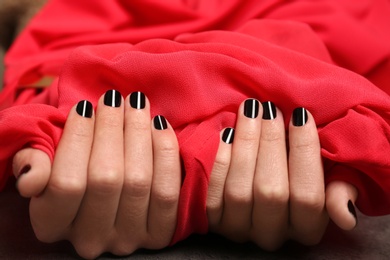 Woman with black manicure holding red fabric, closeup. Nail polish trends