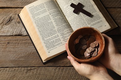 Photo of Donate and give concept. Woman holding bowl of coins. Bible and cross on wooden table, top view