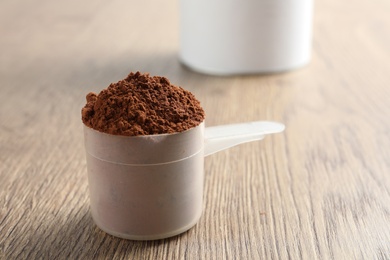 Photo of Scoop of chocolate protein powder on wooden table