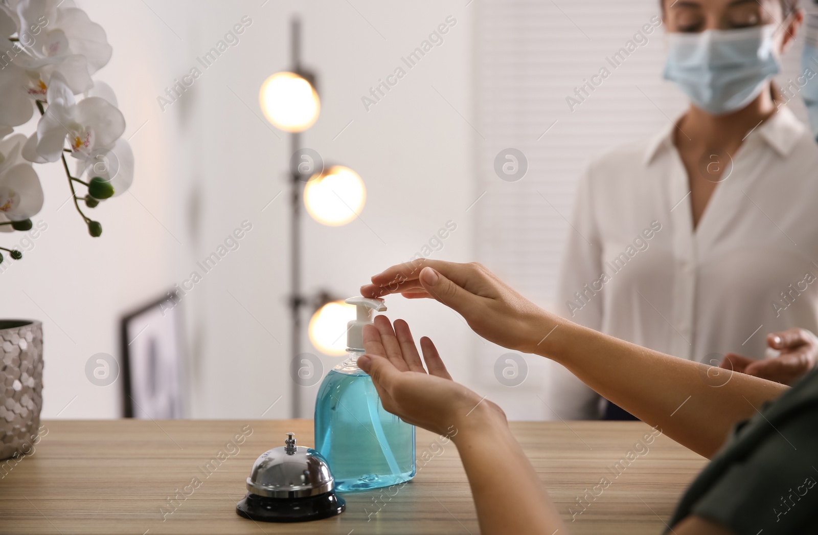 Photo of Woman applying antiseptic gel at hotel reception, closeup