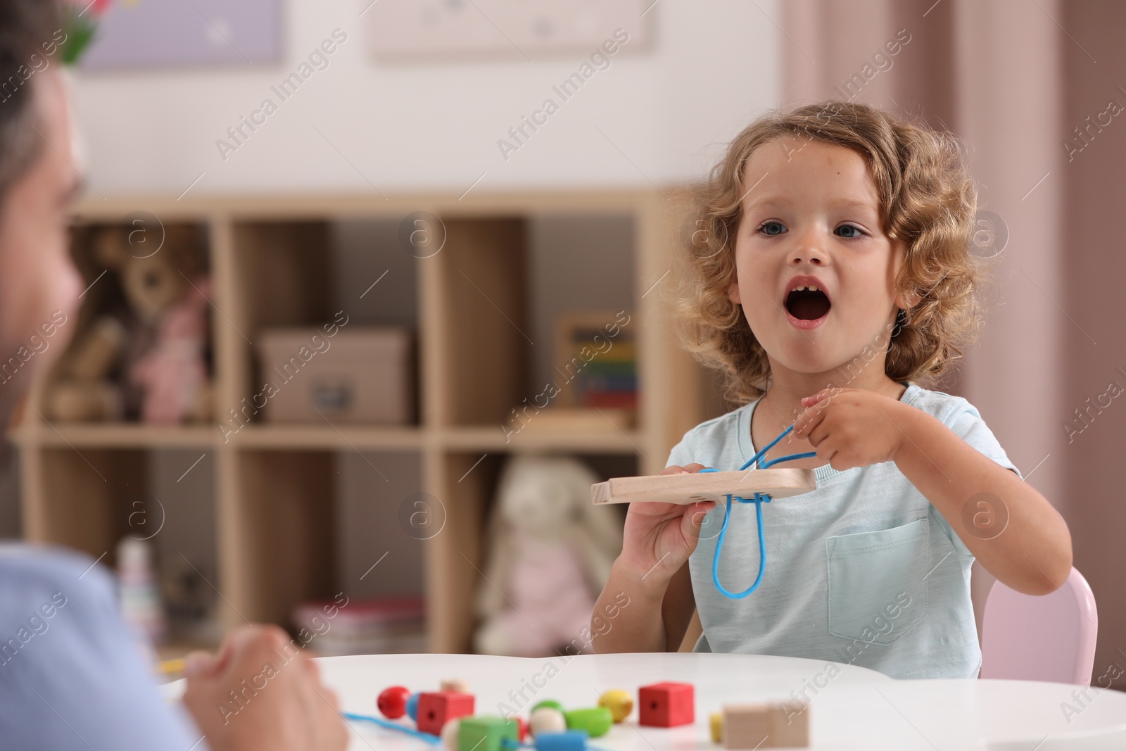 Photo of Motor skills development. Father and little daughter playing with wooden lacing toy at white table indoors