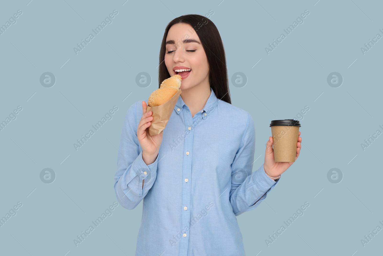 Photo of Young female intern with croissant and cup of drink on grey background