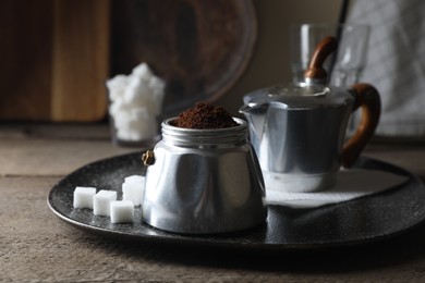 Ground coffee in moka pot and sugar cubes on wooden table, closeup