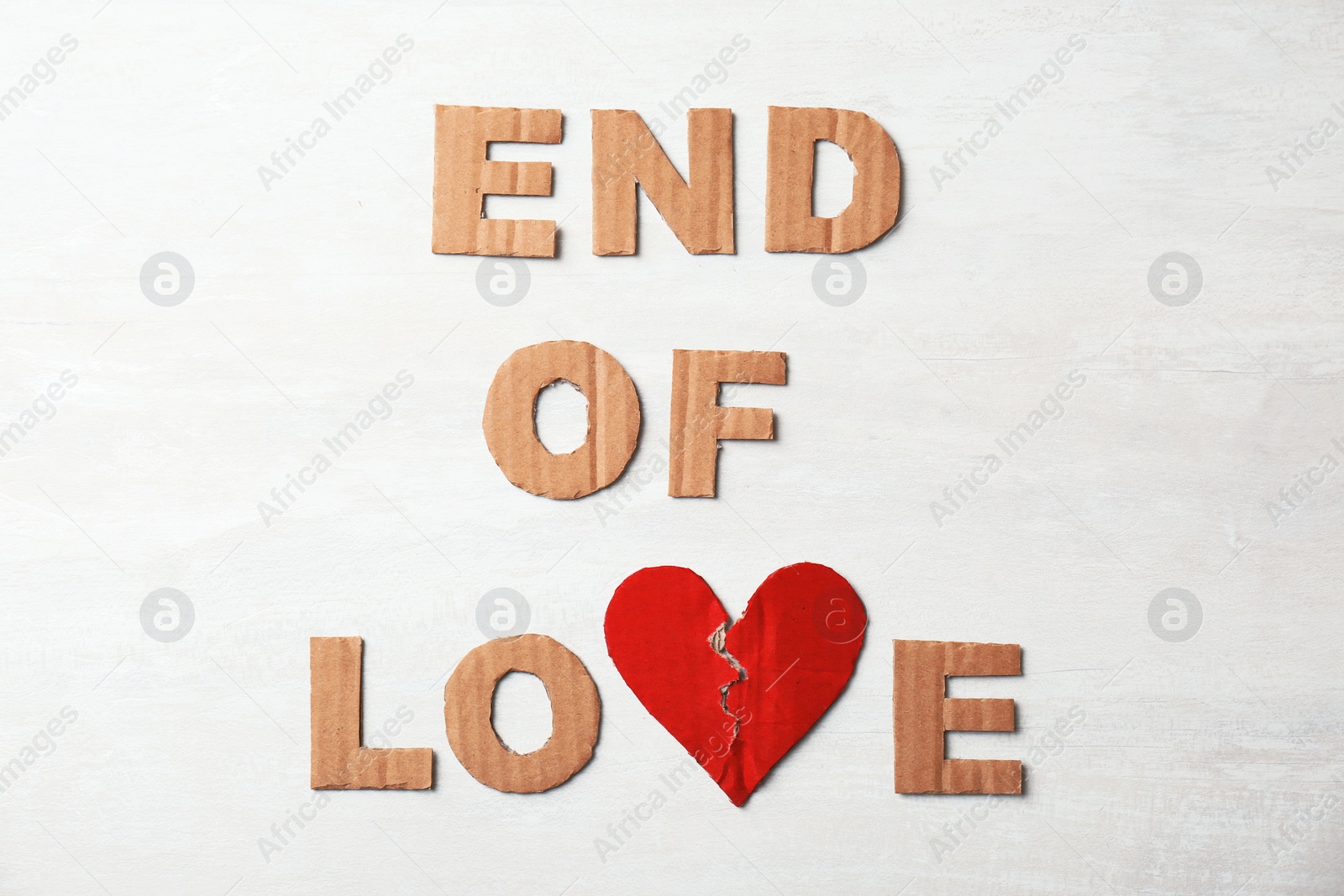Photo of Phrase "End of love" with torn cardboard heart and letters on light background, top view. Relationship problems