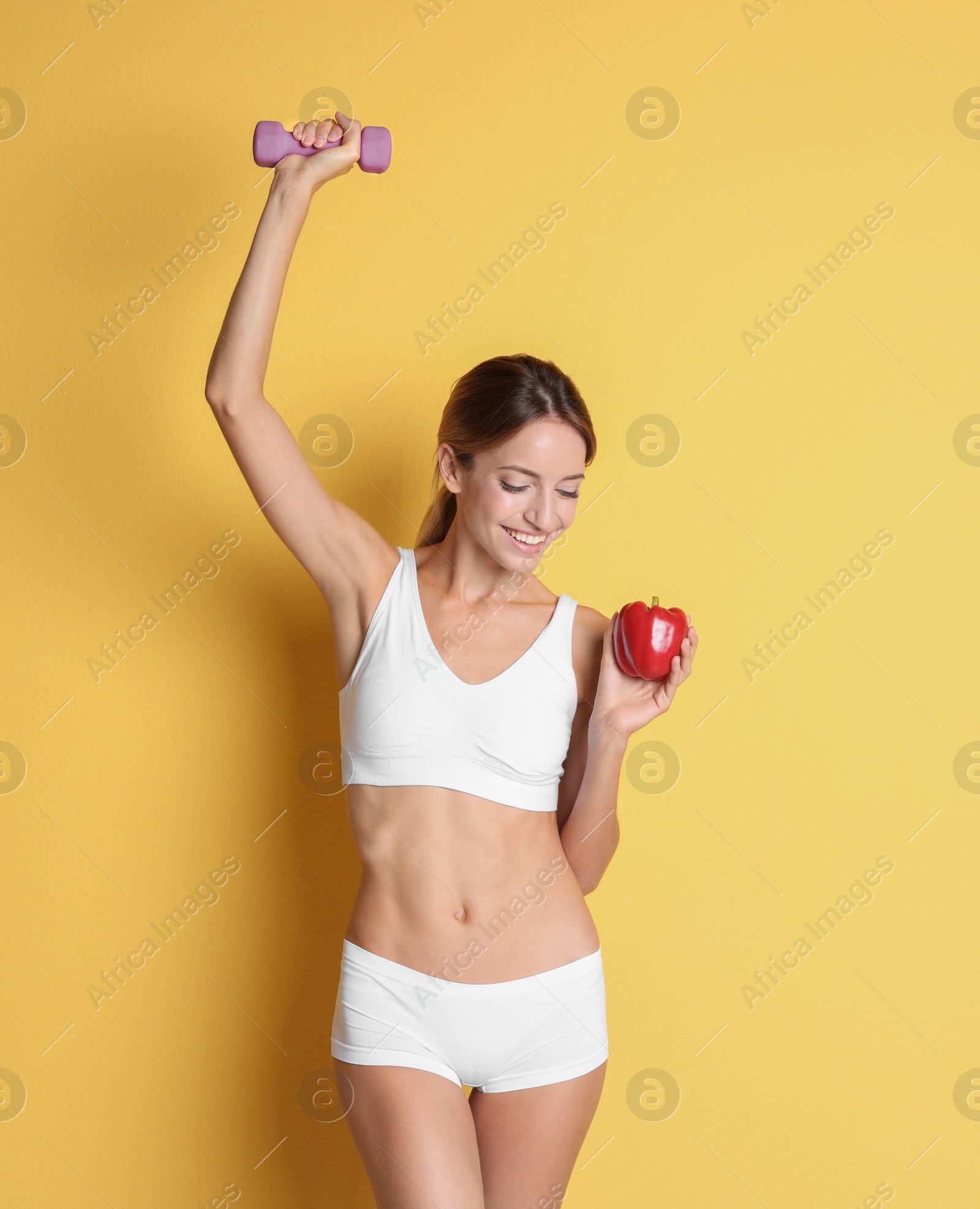 Photo of Happy slim woman in underwear with bell pepper and dumbbell on color background. Weight loss diet