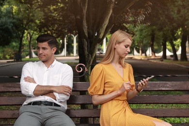 Photo of Young woman with smartphone ignoring her boyfriend in park. Boring date