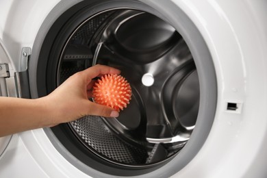 Photo of Woman putting dryer ball into washing machine, closeup