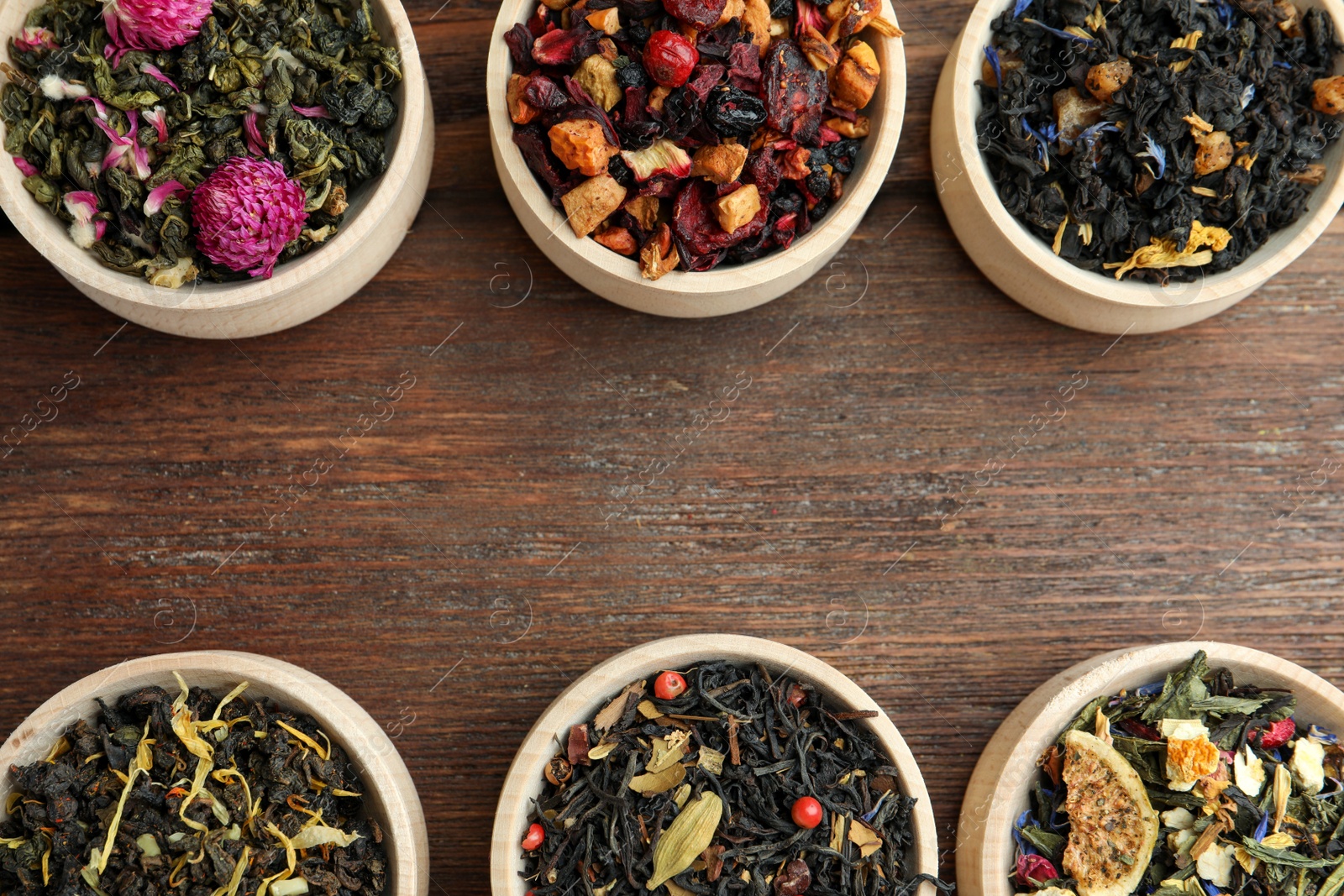 Photo of Different kinds of dry herbal tea in bowls on wooden table, flat lay. Space for text