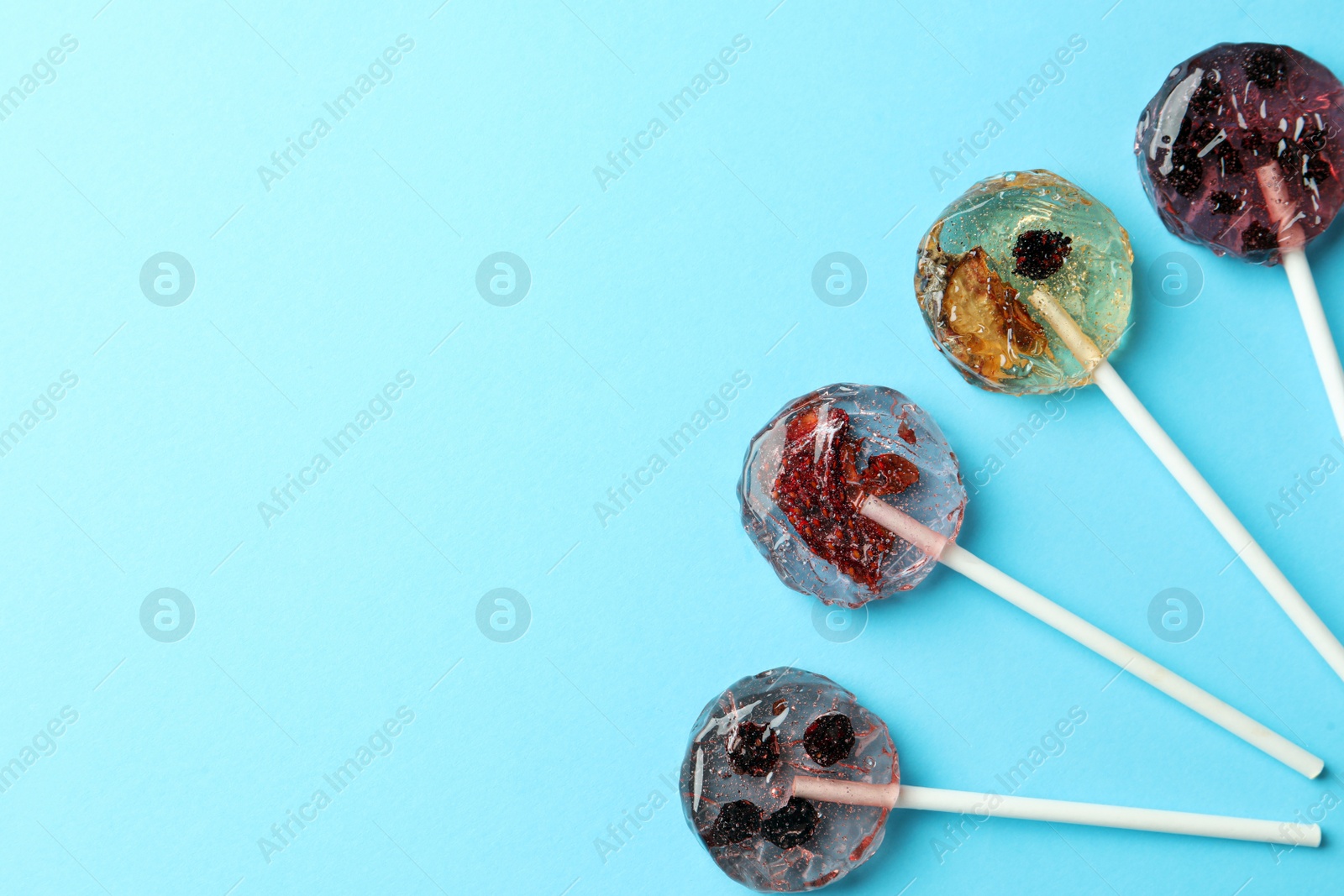 Photo of Sweet colorful lollipops with berries on light blue background, flat lay. Space for text