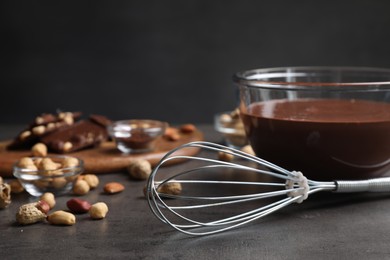 Photo of Whisk, bowl of chocolate cream and nuts on gray table, closeup. Space for text