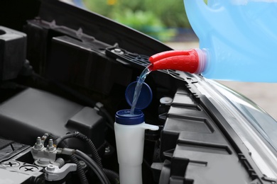 Photo of Man pouring liquid from plastic canister into car washer fluid reservoir, closeup