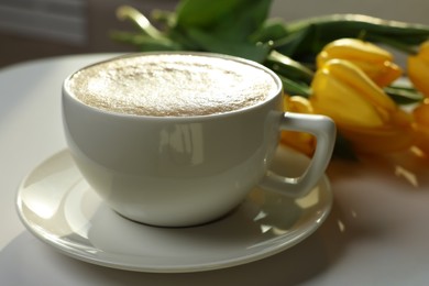 Photo of Morning coffee and flowers on white table indoors, closeup