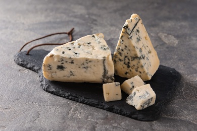 Photo of Slate board with delicious blue cheese on stone surface