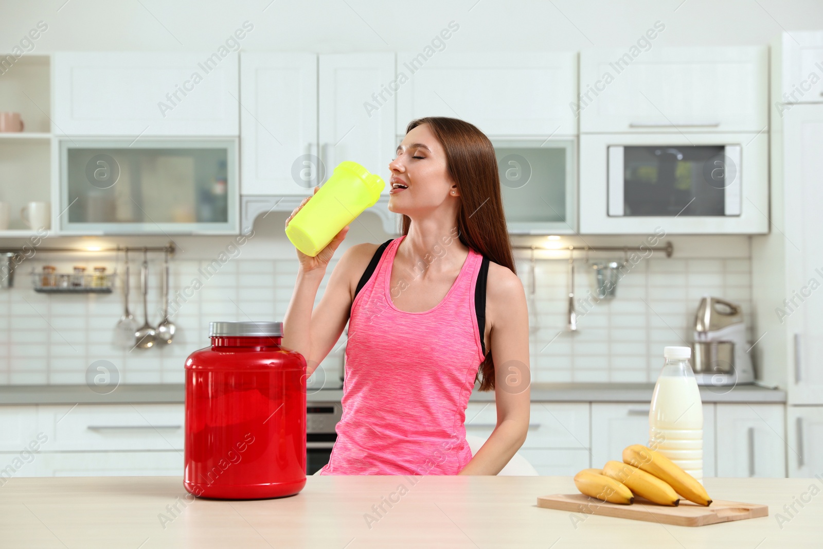 Photo of Young woman drinking protein shake in kitchen