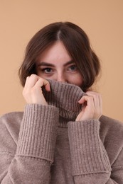 Portrait of beautiful young woman in warm sweater on brown background