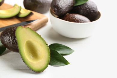 Whole and cut avocados with green leaves on white table