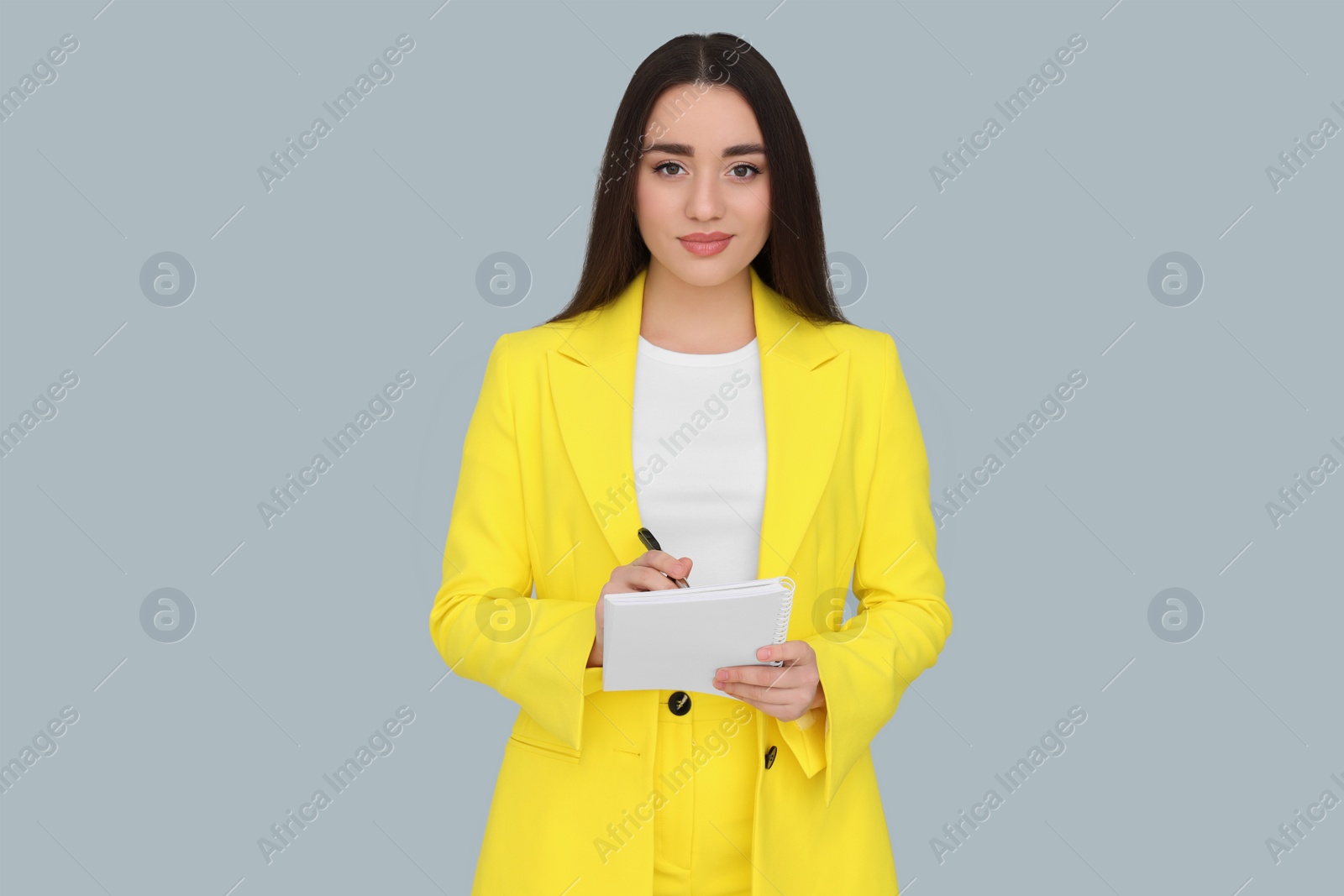 Photo of Young female intern with pen and notebook on grey background