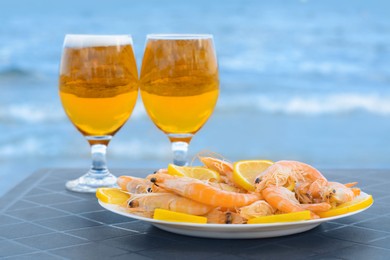 Photo of Cold beer in glasses and shrimps served with lemon on beach