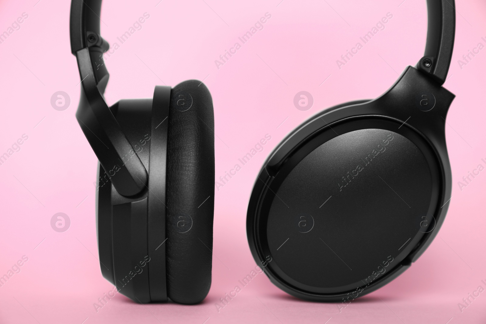 Photo of Modern wireless headphones on pink background, closeup