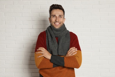 Photo of Happy young man in scarf and warm sweater near white brick wall. Winter season