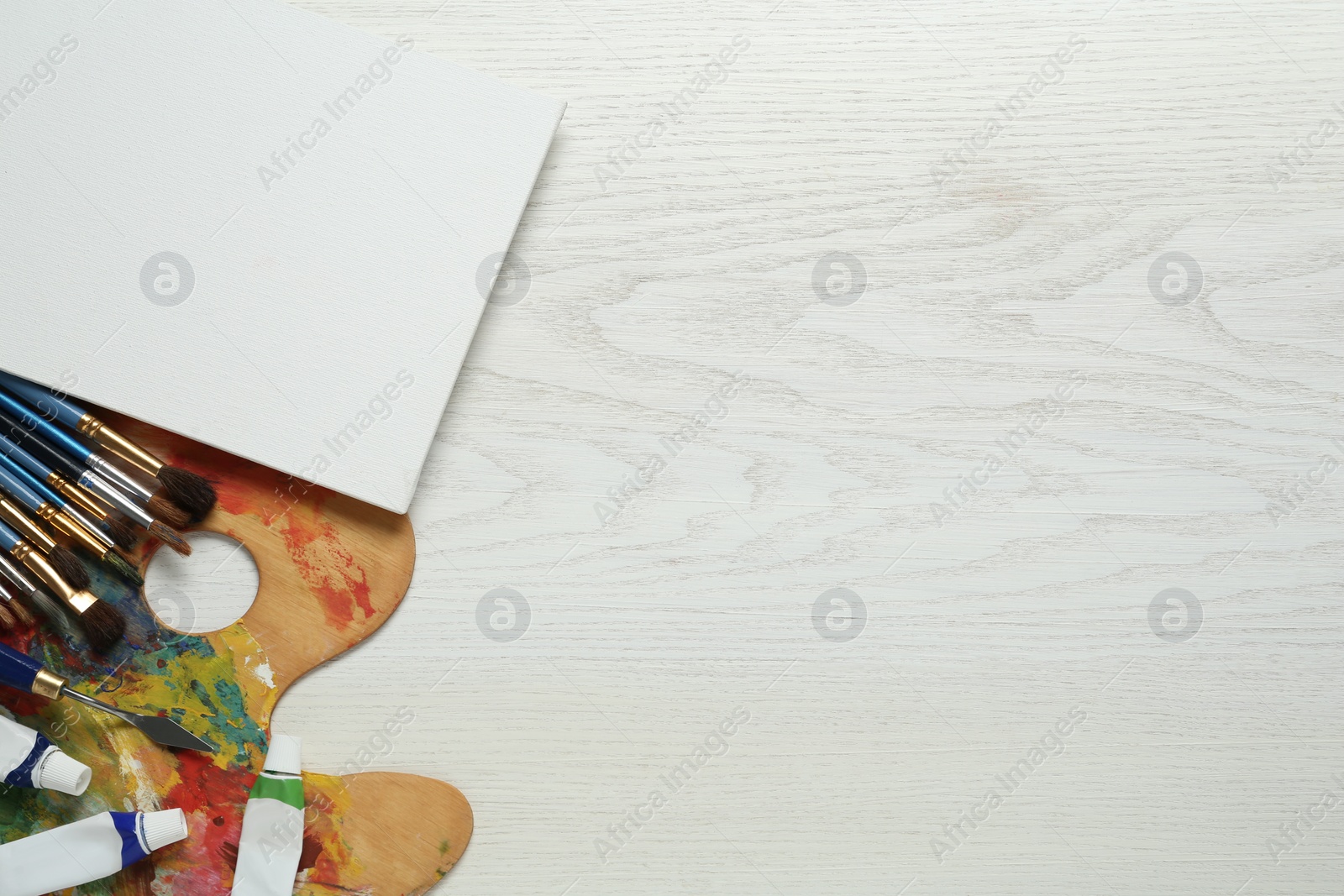 Photo of Blank canvas, brushes, palette and paints on white wooden table, flat lay. Space for text