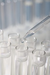 Photo of Laboratory analysis. Dripping liquid from pipette into glass test tube on blurred background, closeup