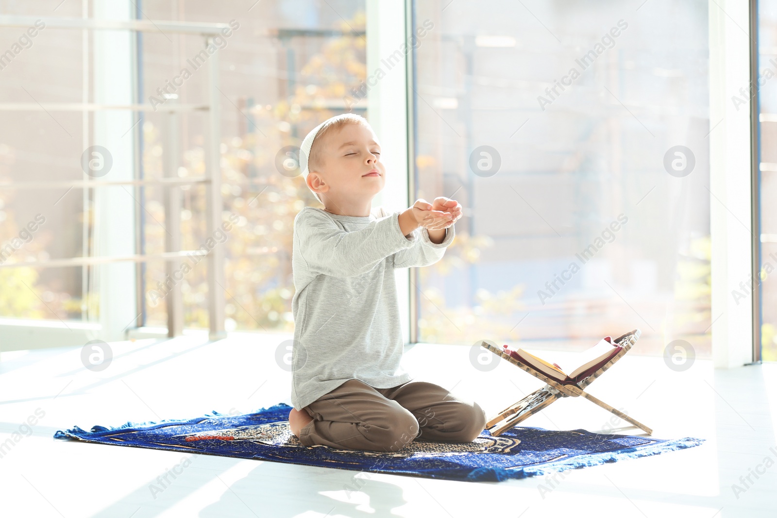 Photo of Little Muslim boy with Koran praying on rug indoors